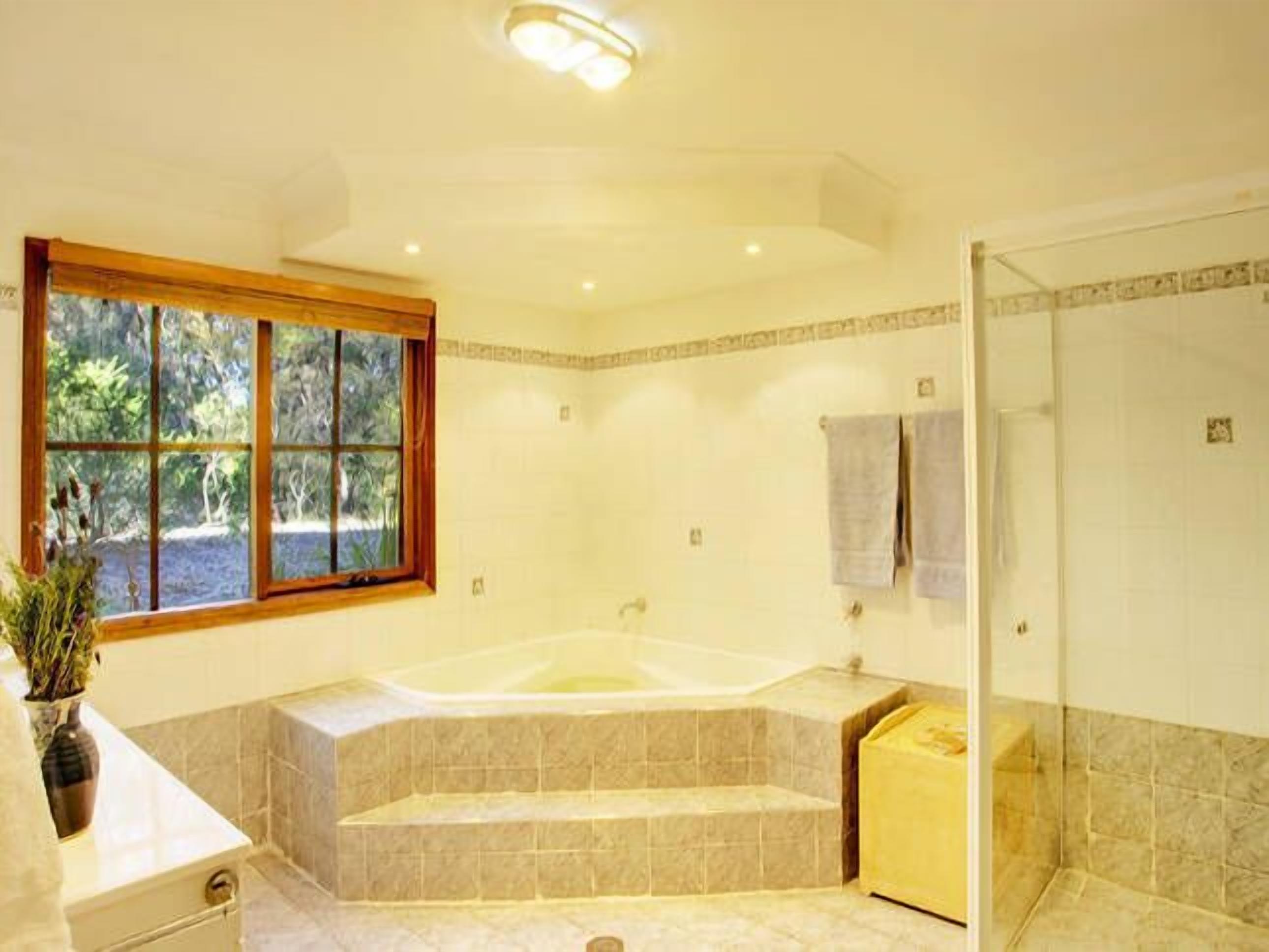 A spacious bathroom with a large bathtub, a shower area, and a window providing a view of greenery.
