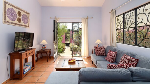 Ein Wohnzimmer mit einer Couch, einem Couchtisch, einem Fernseher und Blick durch eine offene Tür auf einen Garten.