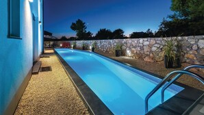 Une piscine bordée d’un mur en pierre et agrémentée de plantes en pot, entourée d’une zone recouverte de galets.
