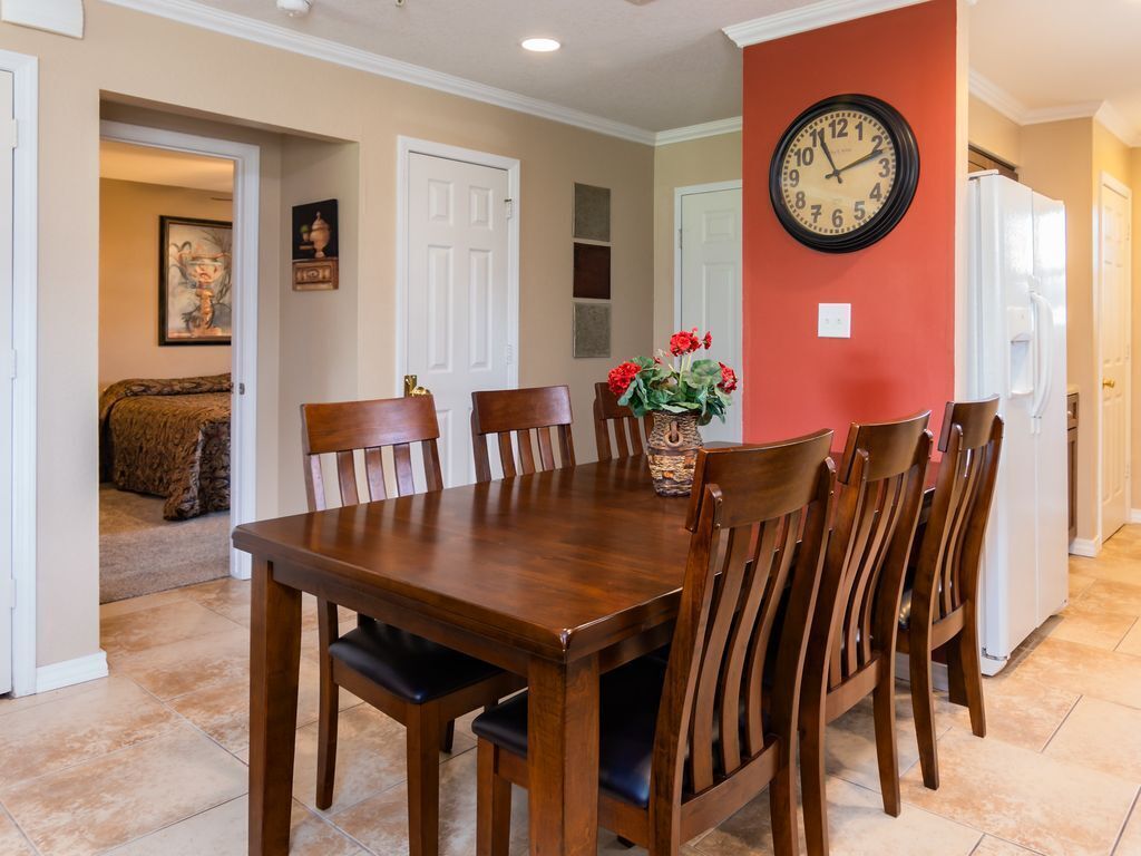 A dining area with a wooden table and chairs, a clock on the wall, and a vase with flowers.
