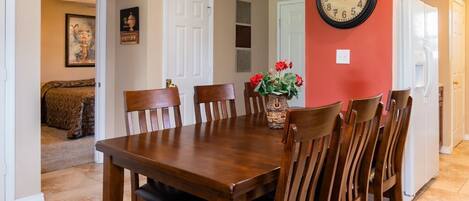 A dining area with a wooden table and chairs, a clock on the wall, and a vase with flowers.