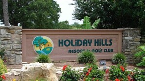 Señal para Holiday Hills Resort & Golf Club con un logotipo que muestra un árbol y un paisaje.