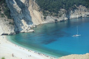 Une plage côtière aux eaux turquoise et limpides, avec un rivage sablonneux et des falaises rocheuses.