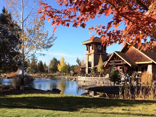A lodge with a stone tower, a pond, and autumn foliage.