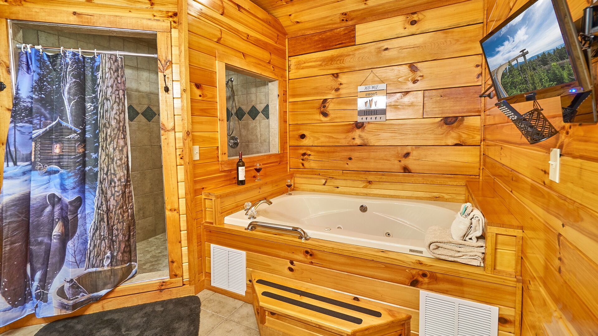 A wooden cabin interior with a large bathtub, a shower area, and a television mounted on the wall.