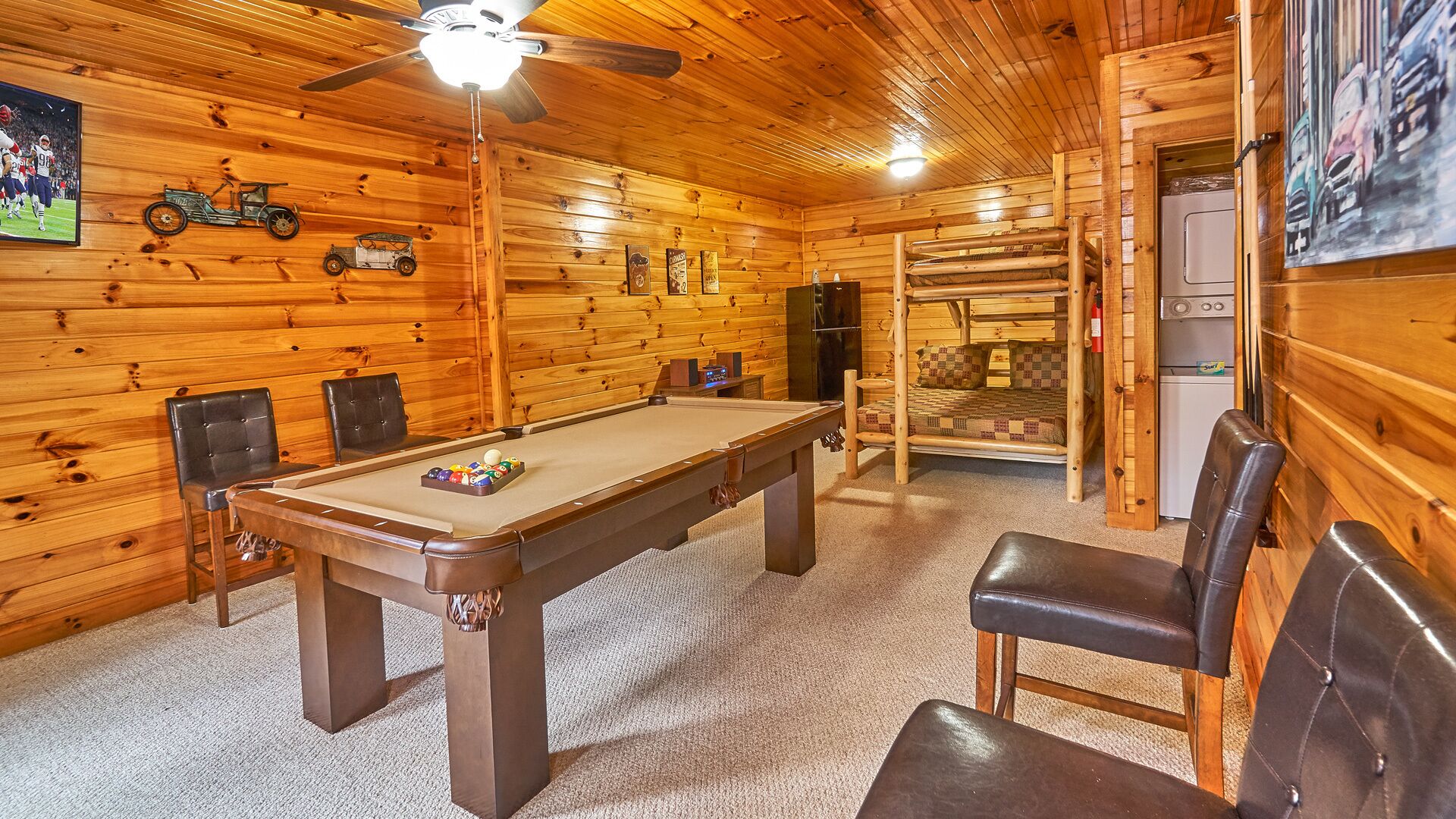 Une table de billard avec des chaises, un ventilateur de plafond et des murs en bois ornés de divers éléments décoratifs.