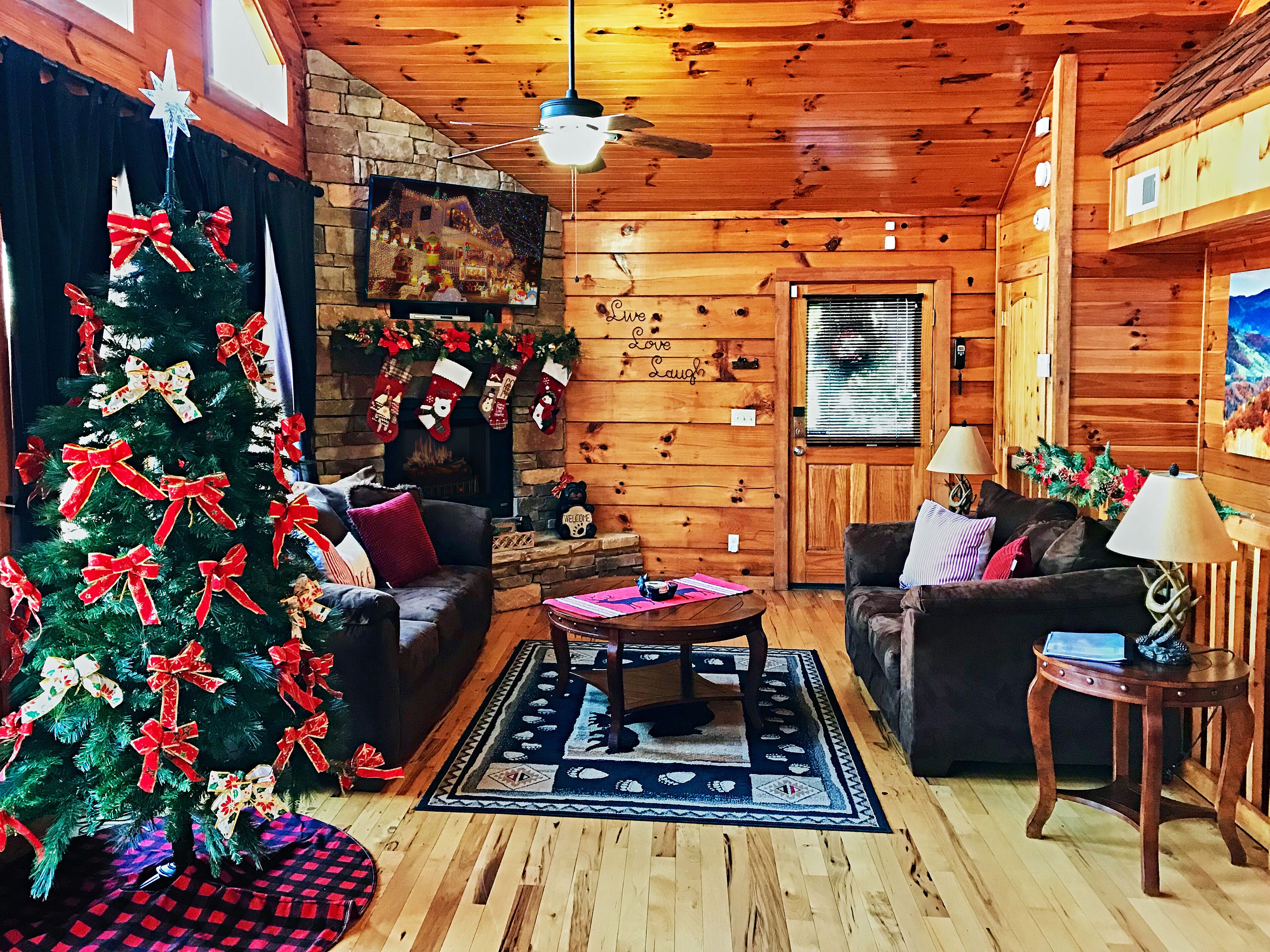 A cozy cabin interior with a fireplace, a Christmas tree, and a comfortable seating area.