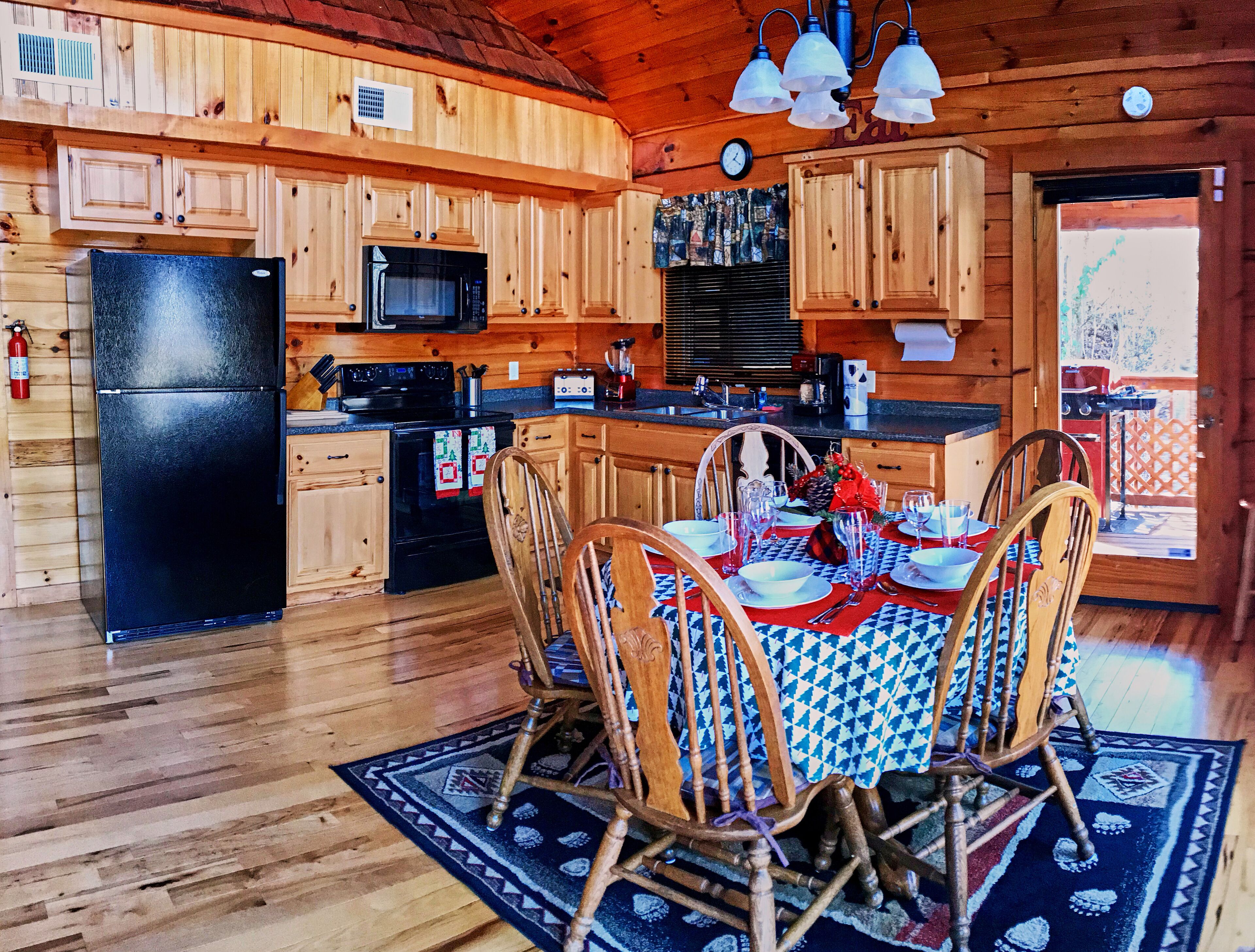 A wooden cabin kitchen with a dining area, equipped with a refrigerator, stove, microwave, and sink.