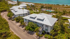 Un resort costero con varias edificaciones blancas, vista despejada del océano y un paisaje bien cuidado con palmeras.