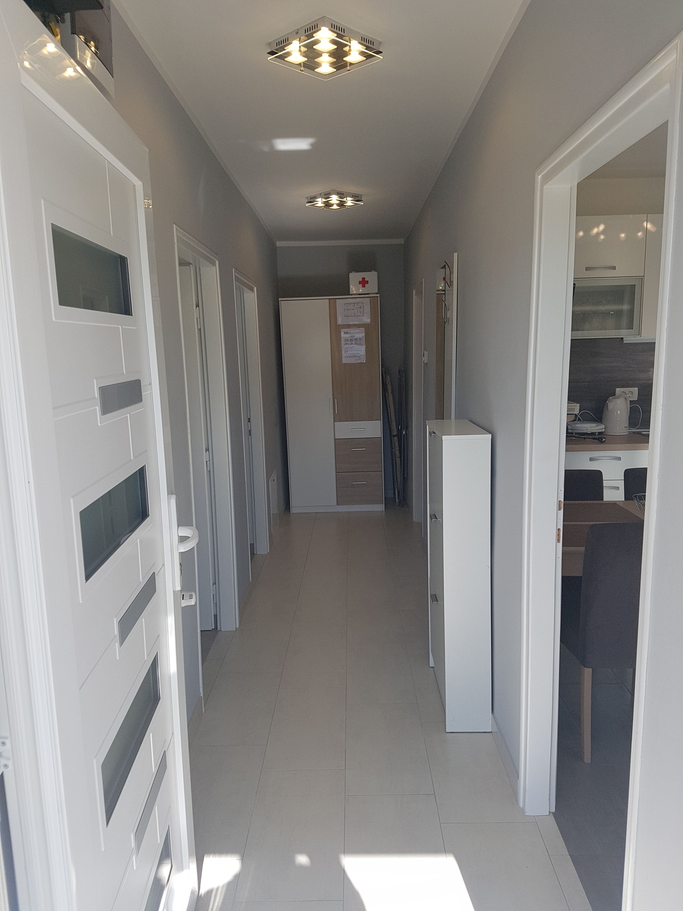 A narrow hallway with white doors, a kitchenette area, and a ceiling light fixture.