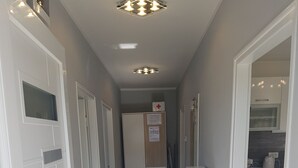 Un couloir étroit avec des portes blanches, un coin cuisine et un luminaire au plafond.