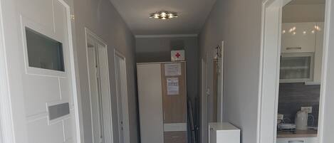 A narrow hallway with white doors, a kitchenette area, and a ceiling light fixture.
