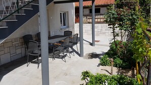 Un espace extérieur aménagé en terrasse, avec une table et des chaises, un escalier et un jardin où poussent différentes plantes.