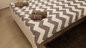 Une chambre à coucher comprenant un lit, un radiateur, une fenêtre avec des stores, une table de chevet avec une lampe et un tableau accroché au mur.