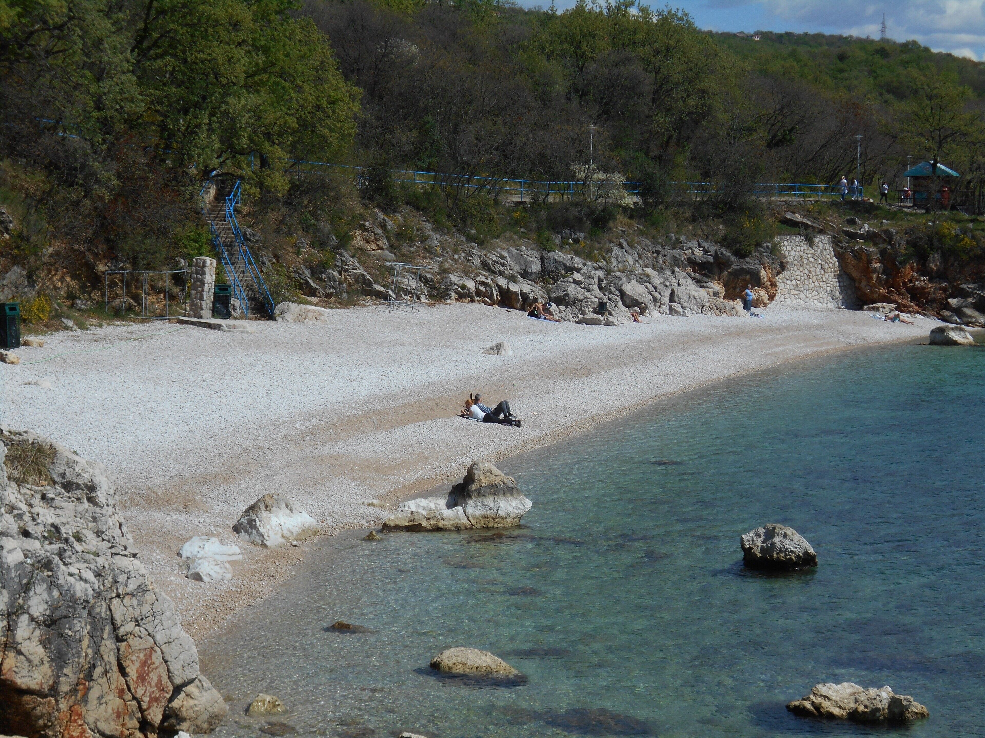 Une plage avec une eau claire, des affleurements rocheux et quelques personnes.
