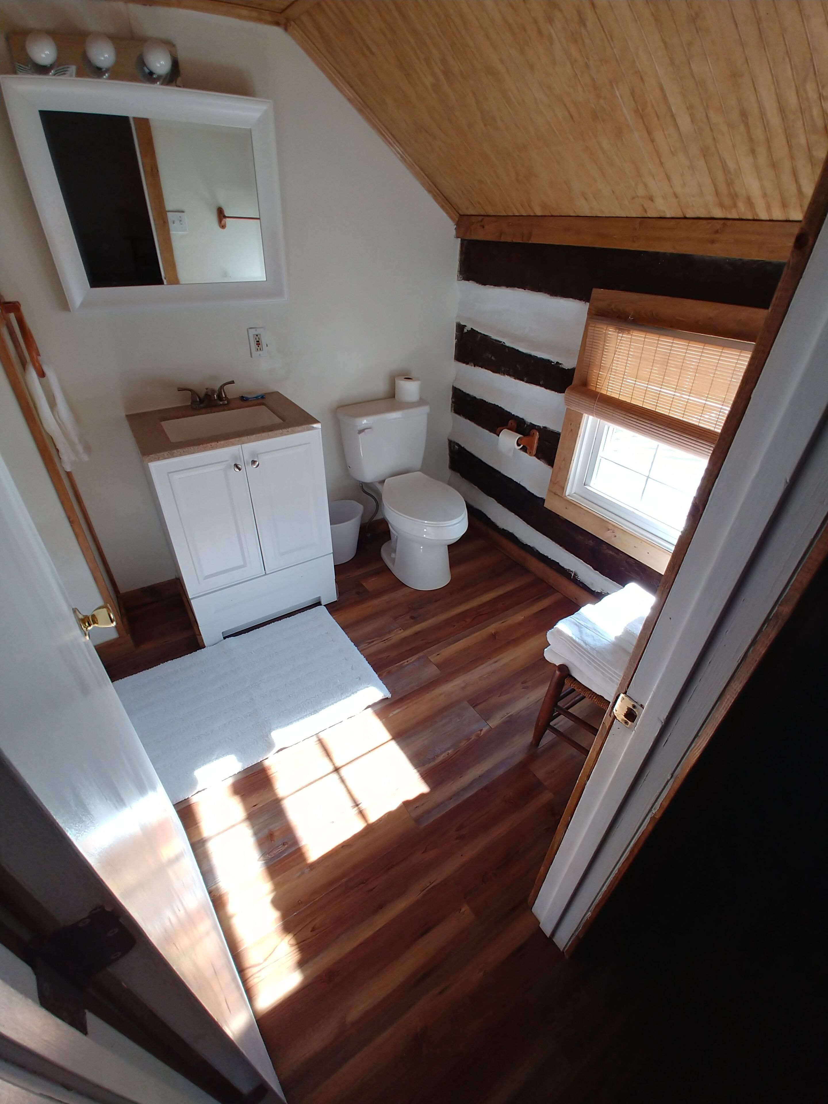 A small, compact bathroom with a wooden floor, a white sink, a toilet, and a mirror above the sink.