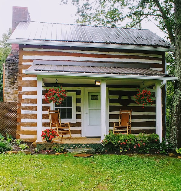Une cabane en rondins avec un porche, deux fauteuils à bascule et des fleurs rouges.