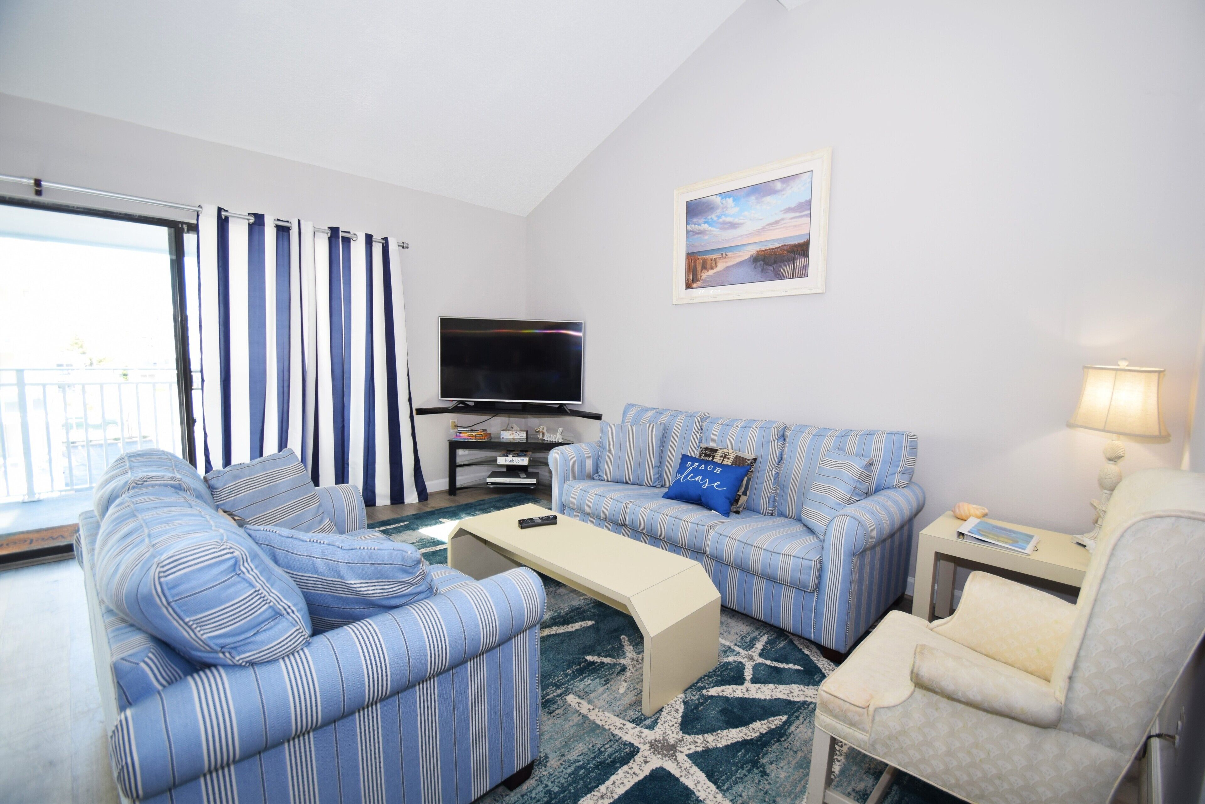 A living room with striped sofas, a coffee table, a TV, and a lamp.