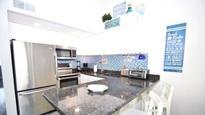 A modern kitchen with stainless steel appliances, a granite countertop, and a backsplash with blue tiles. - Surfside 60 Unit 303-Oceanside 60th St, Free WiFi, W/D, AC (Ocean City)