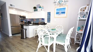 A modern kitchen with stainless steel appliances, a dining area with white wicker chairs, and a beach-themed decor. - Surfside 60 Unit 303-Oceanside 60th St, Free WiFi, W/D, AC (Ocean City)