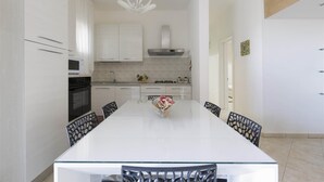 Una cocina moderna con armarios blancos, una isla central y un comedor con mesa y sillas de vidrio.