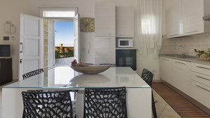 Una cocina moderna con una mesa de comedor de vidrio, sillas negras, un reloj grande y vistas al exterior.