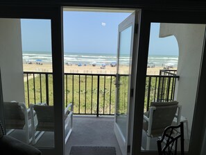 A balcony with a view of the beach, two chairs, and a glass door. - Beach facing balcony, Fully furnished, Beach supplies, sleeps 6. pool & hot tub (South Padre Island)