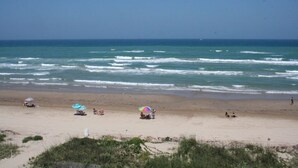 A beach with waves, umbrellas, and people.