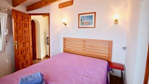 A bedroom with a wooden headboard, a pink bedspread, and a painting on the wall.