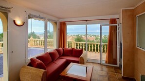 A balcony with a red sofa, a wicker chair, and a glass-top table.