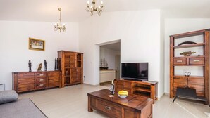 Ett modernt vardagsrum med ett TV-bord i trä, en soffa och ett soffbord. Det finns träskåp med dekorativa föremål och en kristallkrona.