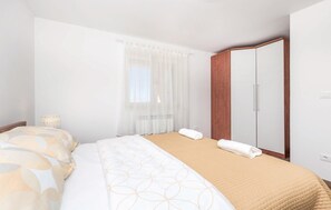 A hotel room with a bed, a wooden wardrobe, a window with sheer curtains, and a bedside lamp. - 1 bedroom beautiful apartment in Matulji (Matulji)
