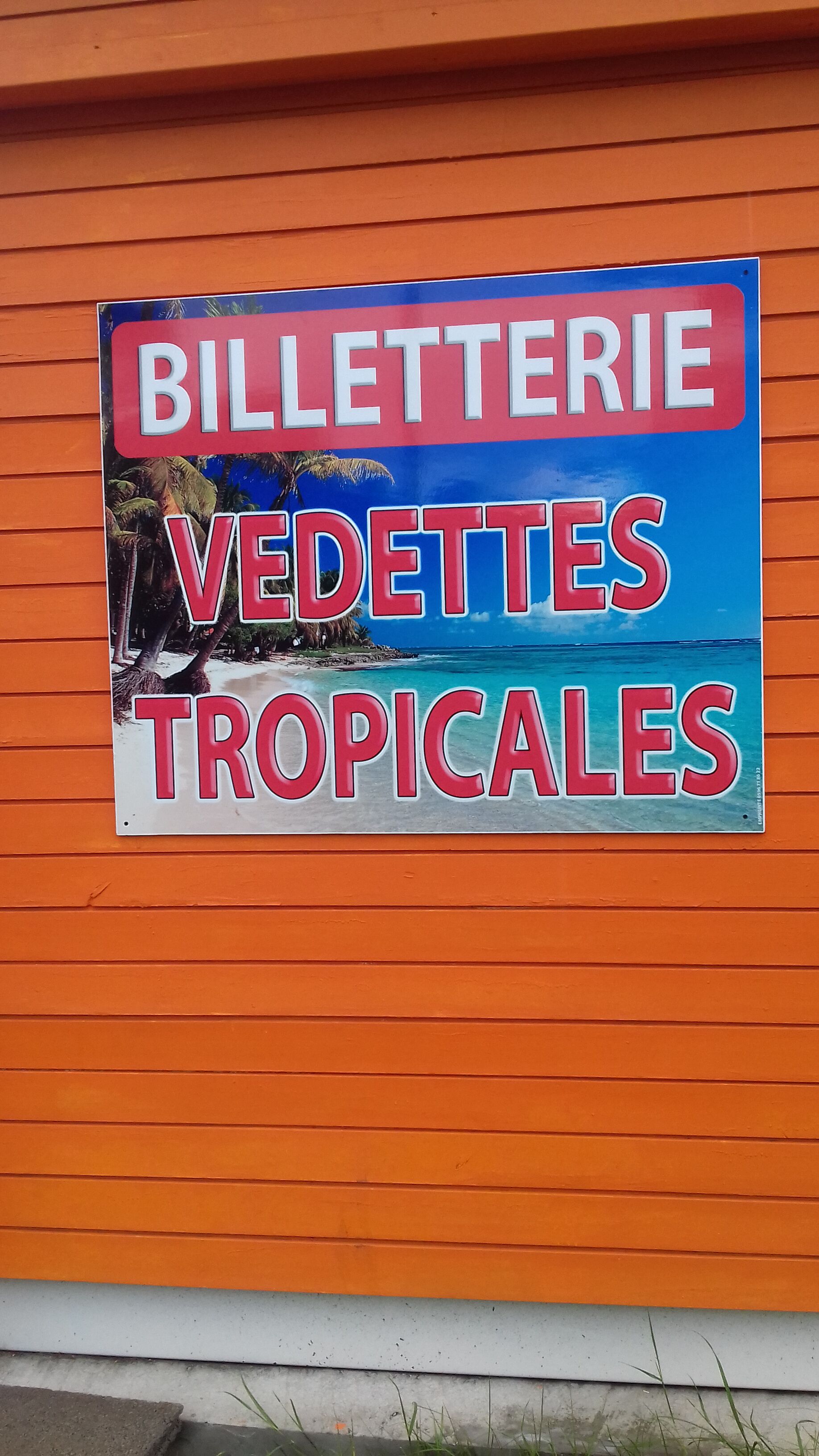A sign with the text "BILLETERIE VEDETTES TROPICALES" on an orange wall.