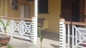 A two-story building with a tiled roof, a balcony with a white railing, and a door marked with the number 28. - Your studio in the Tropics of Martinique. 5 minutes walk from the beach! (Les Trois-Îlets)