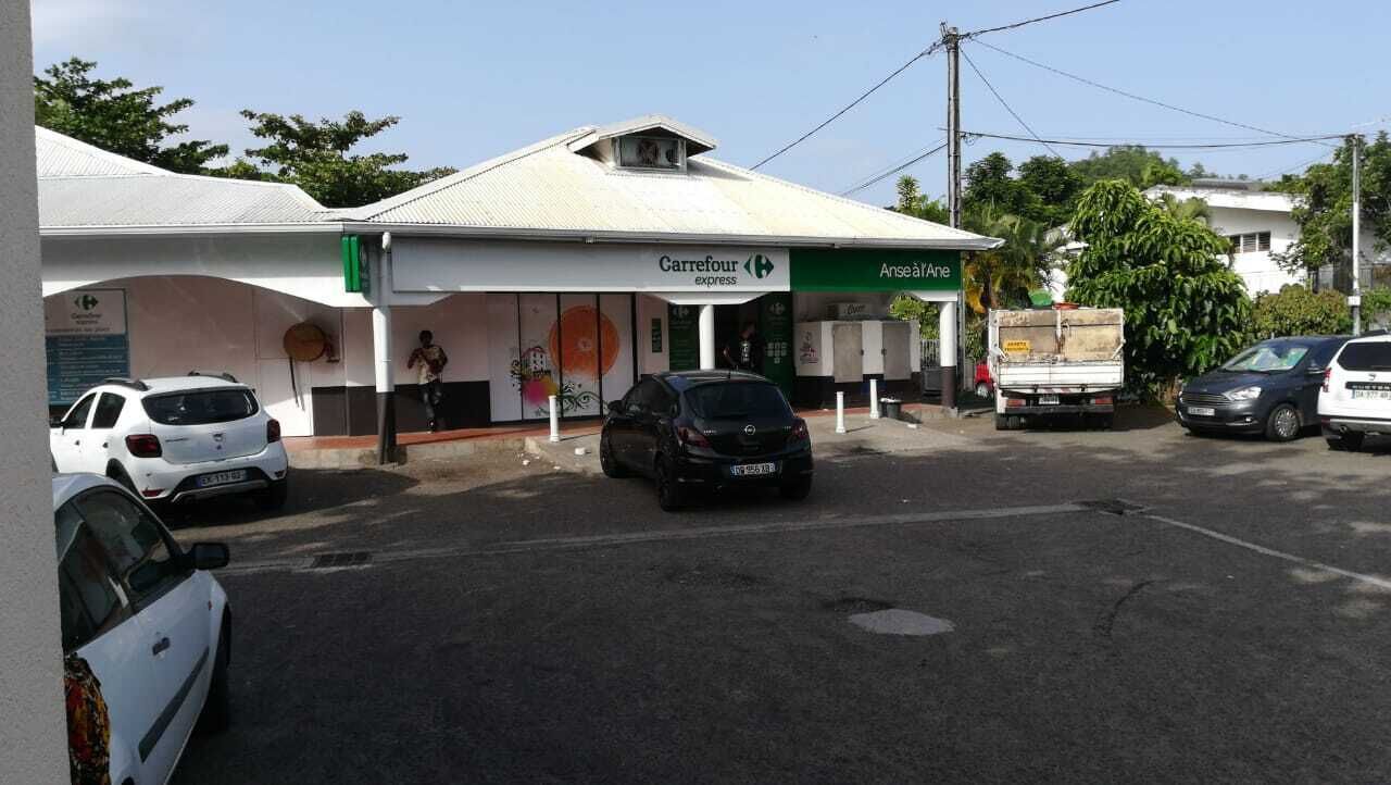 A Carrefour Express store with a white facade and green signage, parked cars, and a truck in the parking lot.