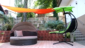 Un patio con un sofá redondo de mimbre, una silla colgante y una sombrilla verde.