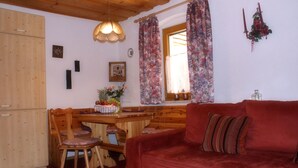 Una habitación acogedora con una mesa de comedor de madera, sillas, un sofá rojo y una ventana con cortinas florales.