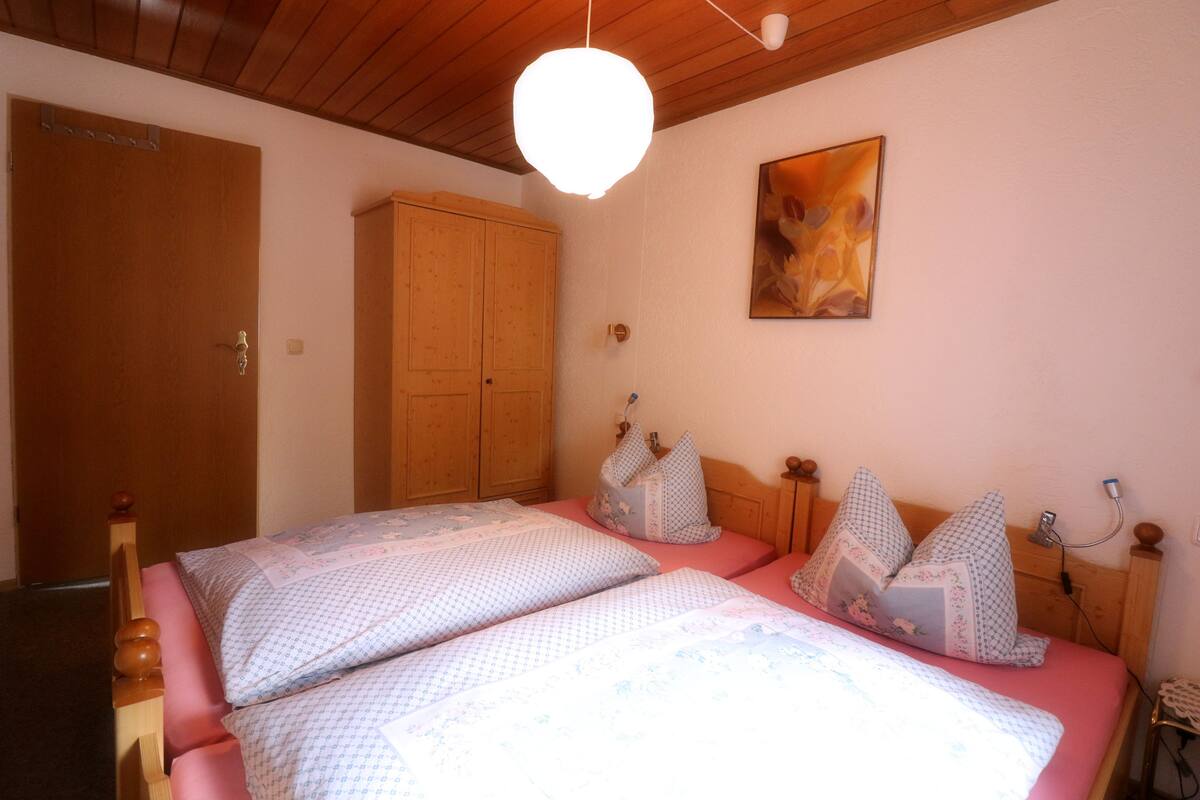 A bedroom with two beds, wooden wardrobe, and a ceiling light fixture.