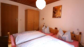 A bedroom with two beds, wooden wardrobe, and a ceiling light fixture.