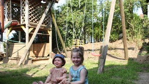 Dos niños sentados sobre la hierba cerca de una estructura de juego de madera con un tobogán.