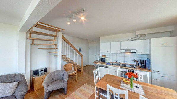 A modern kitchen with white cabinets, a wooden dining table, and a staircase leading to the upper floor.