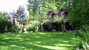 Et traditionelt hus med saddeltag, omgivet af frodig vegetation og en velplejet græsplæne.