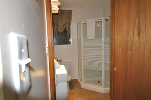 Ein Badezimmer mit Toilette, Duschkabine und einem Fenster mit Vorhängen.