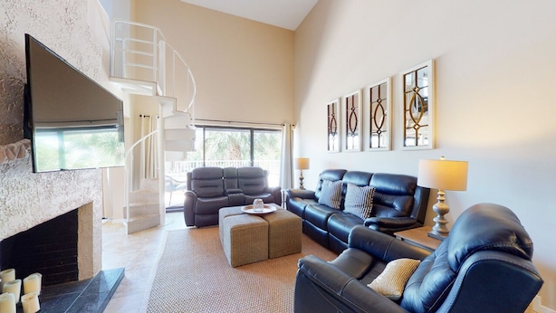 Un salon spacieux doté d’une cheminée, d’un escalier, d’un grand téléviseur à écran plat et d’un coin salon confortable avec un canapé et des fauteuils.