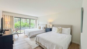 Une chambre d’hôtel avec deux lits, un bureau, une chaise et une grande fenêtre donnant sur un paysage verdoyant.