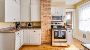 A kitchen with white cabinets, a brick accent wall, a microwave, an oven, and a coffee maker.