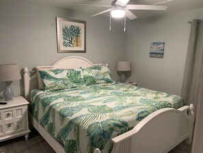 A bedroom with a bed, a nightstand, a ceiling fan, and wall art.