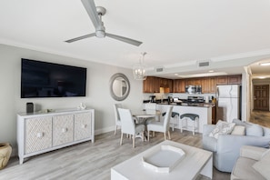A modern kitchen with a dining area, a large flat-screen TV, and a ceiling fan.