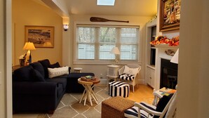 Un salon chaleureux avec un canapé bleu foncé, un pouf à rayures, un fauteuil à bascule blanc et une cheminée.