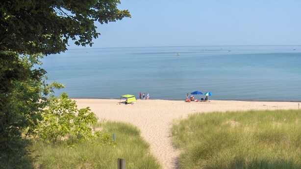 Une plage avec un sentier sablonneux menant à l’eau, une tente verte et un parasol bleu.